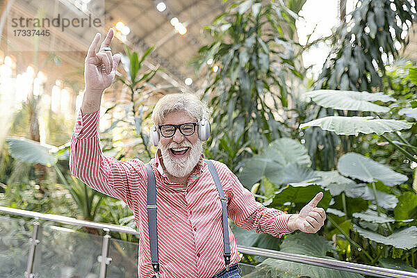 Glücklicher reifer Mann mit Brille tanzt vor Pflanzen