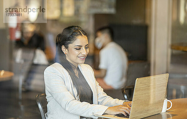 Weibliche Fachkraft  die einen Laptop benutzt  während sie in einem Café sitzt  gesehen durch ein Fensterglas