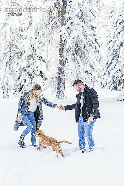 Ehepaar spielt mit Hund im Schnee während des Urlaubs