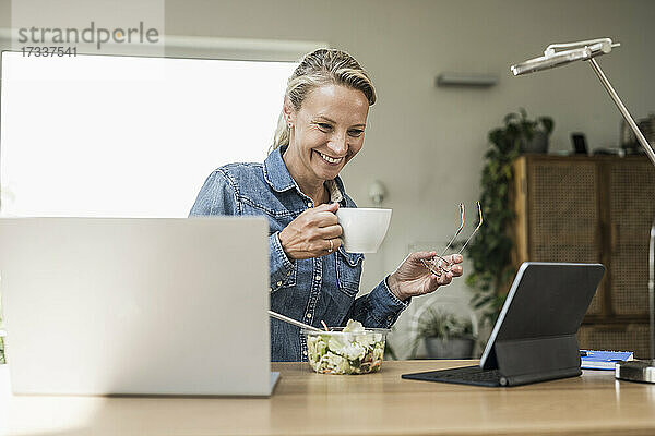 Lächelnde Geschäftsfrau  die Kaffee trinkt und auf ein digitales Tablet schaut