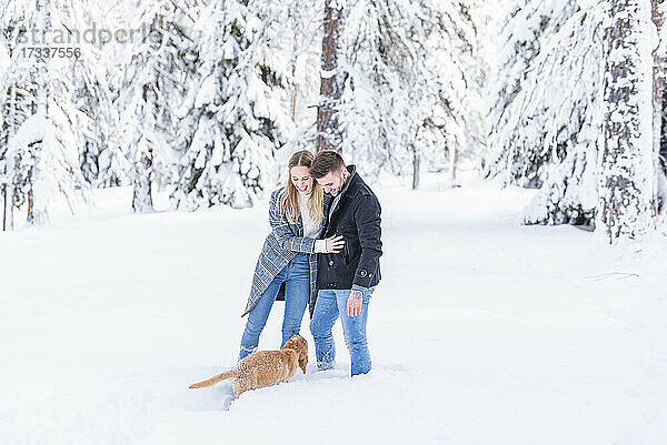 Junges Paar im Schnee stehend mit Hund im Urlaub