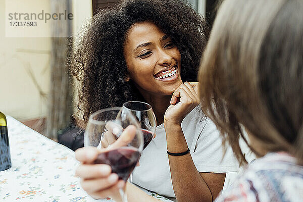 Lächelnde Frau mit Hand am Kinn im Gespräch mit einem Freund auf der Terrasse