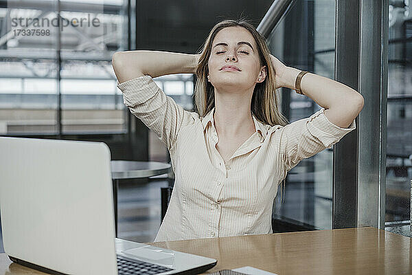 Entspannte Geschäftsfrau sitzt mit den Händen hinter dem Kopf in einem Cafe