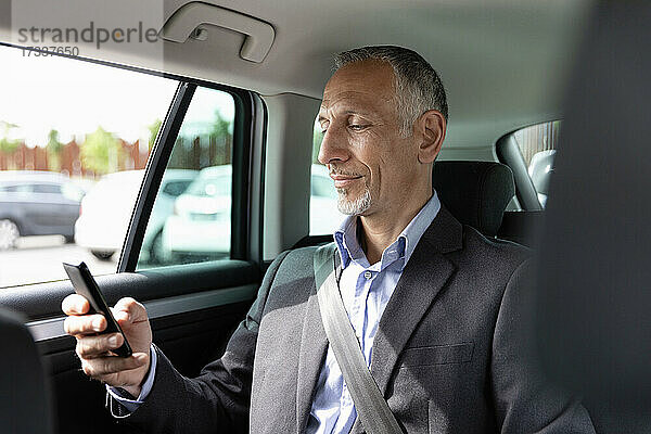 Männlicher Berufstätiger benutzt Smartphone  während er auf dem Rücksitz im Auto sitzt