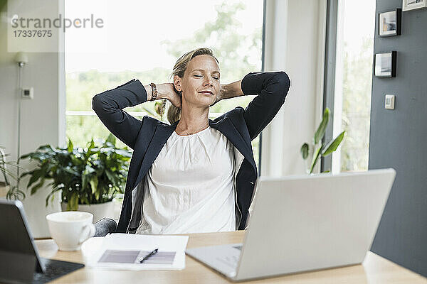 Geschäftsfrau mit Händen hinter dem Kopf beim Sitzen im Büro ruhend