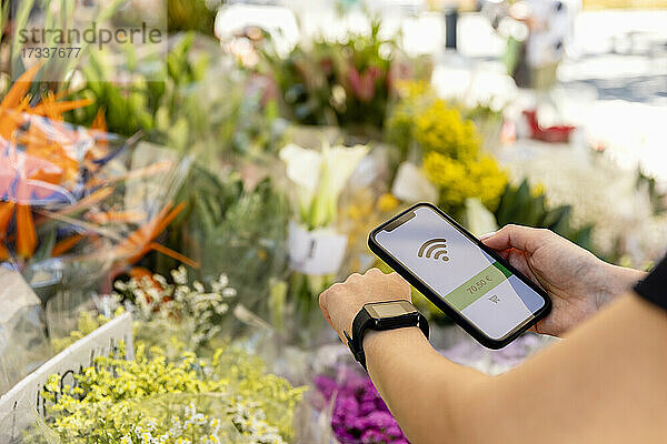 Frau beim kontaktlosen Bezahlen mit Smartwatch und Mobiltelefon im Blumenladen