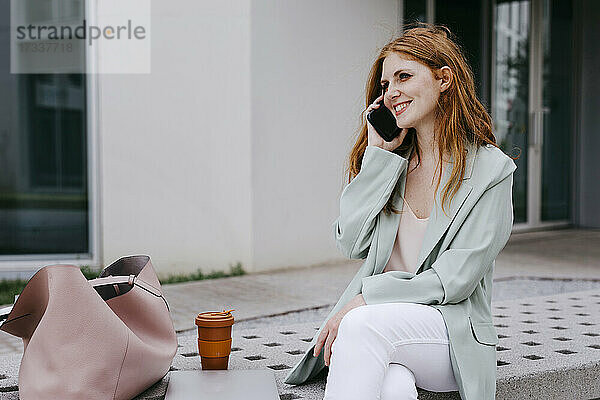 Lächelnde Geschäftsfrau  die auf einer Bank sitzend mit einem Mobiltelefon spricht