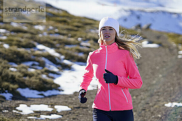Junge Sportlerin läuft im Winter an einem sonnigen Tag auf einem Berg