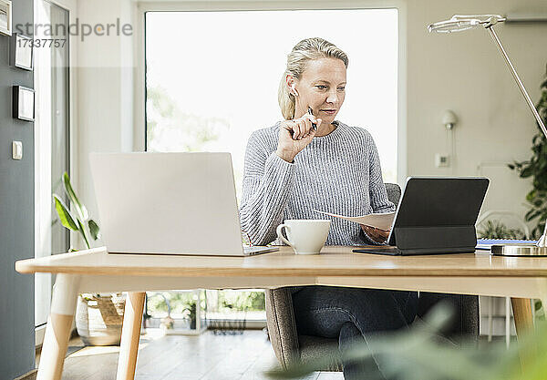 Geschäftsfrau mit digitalem Tablet und Laptop  die Papier bei der Arbeit im Büro zu Hause hält
