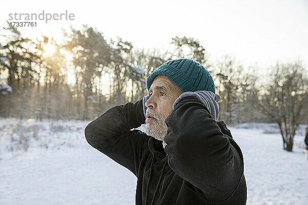Älterer Mann mit Händen hinter dem Kopf und Strickmütze im Winter