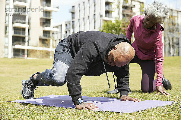 Ältere Frau hilft einem Mann bei einer Übung in einem öffentlichen Park