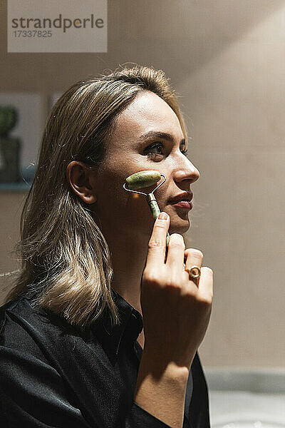 Junge Geschäftsfrau massiert Gesicht mit Jadewalze zu Hause
