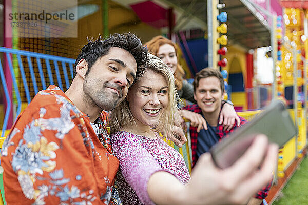Lächelnde Frau nimmt Selfie mit Freunden durch Smartphone im Vergnügungspark