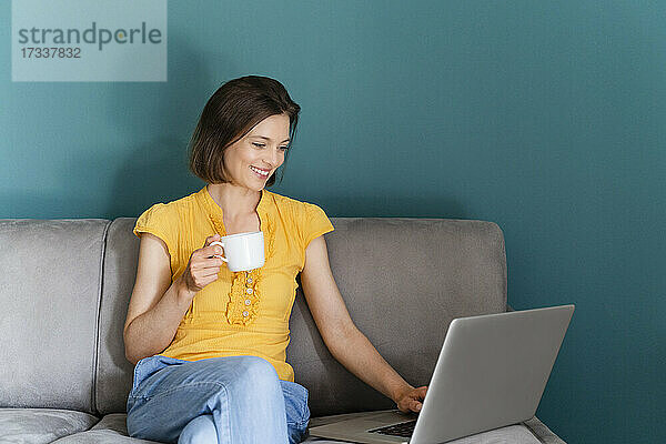 Frau mit Kaffeetasse und Laptop auf dem Sofa sitzend