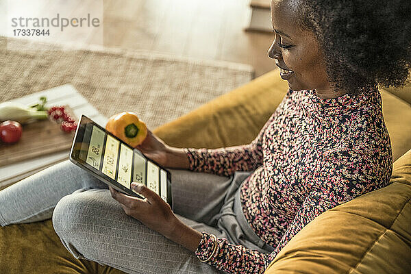 Lächelnde Frau  die zu Hause Gemüsekalorien über ein digitales Tablet zählt