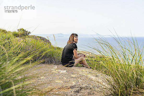 Reife Frau schaut weg  während sie auf einer Klippe sitzt