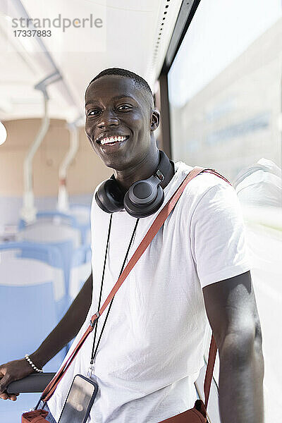 Lächelnder männlicher Profi mit Umhängetasche und Kopfhörern im Bus