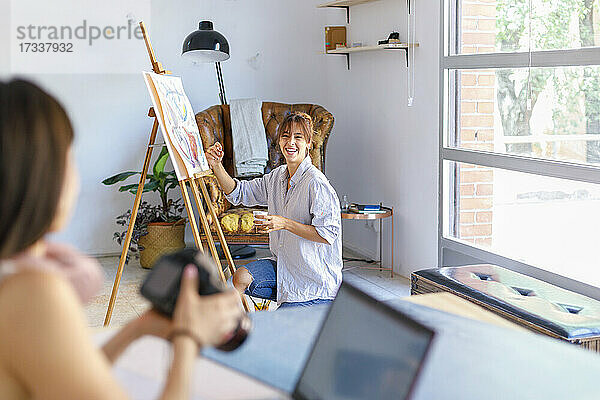 Lächelnde Malerin schaut Fotografenkollege an  der im Studio die Kamera hält