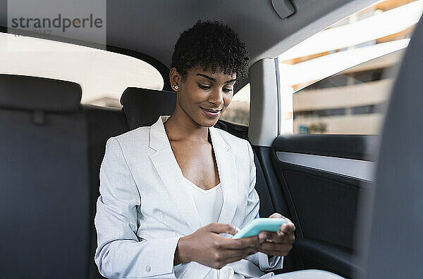 Geschäftsfrau  die im Auto sitzend ihr Smartphone benutzt