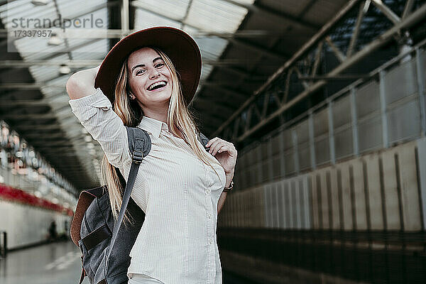 Fröhliche blonde Frau mit Rucksack am Bahnhof