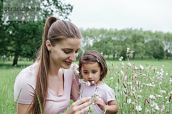 Lächelnde Frau mit Tochter riecht an Blumen im Park