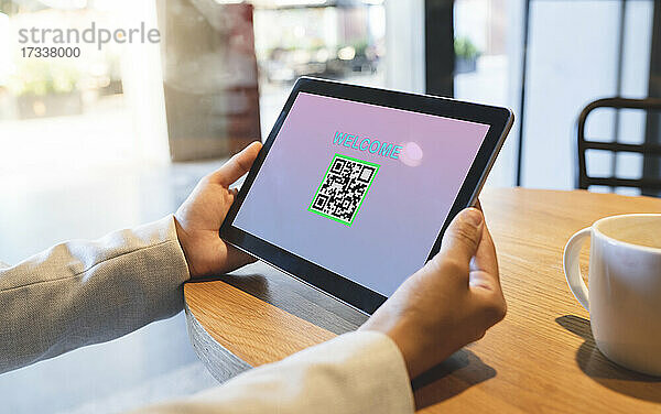Geschäftsfrau hält digitales Tablet mit QR-Code und Begrüßungstext in einem Café