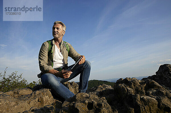 Mann mit digitalem Tablet auf einem Felsen sitzend