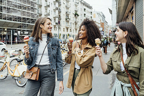 Lächelnde Freunde essen Eis beim Spaziergang in der Stadt Straße