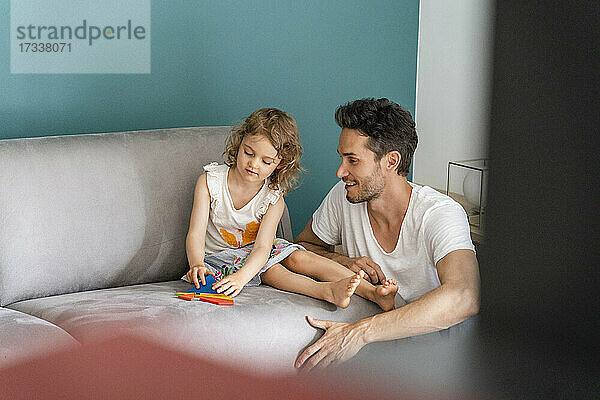 Tochter spielt mit einem Puzzle  während sie neben ihrem Vater im Wohnzimmer sitzt