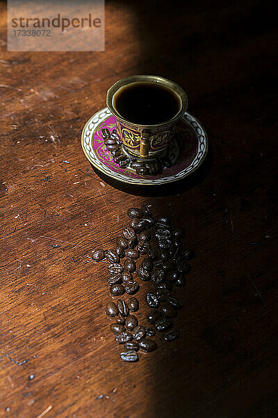 Tasse Kaffee und rohe Kaffeebohnen liegen auf einem schattigen Tisch