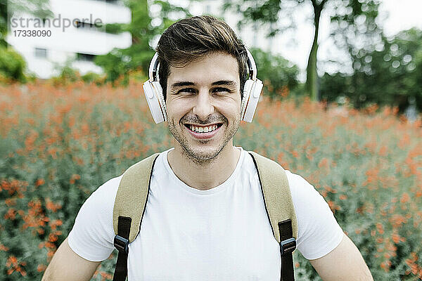 Lächelnder junger Mann hört Musik über Kopfhörer inmitten einer Wiese