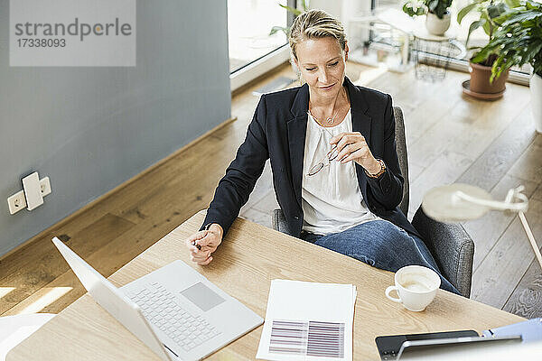 Geschäftsfrau mit Laptop und digitalem Tablet im Büro sitzend