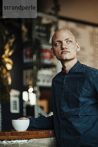 Nachdenklicher männlicher Café-Besitzer  der mit einer Kaffeetasse in der Hand wegschaut