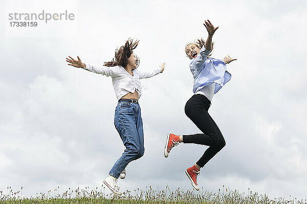 Unbekümmerte junge Freundinnen springen auf Gras