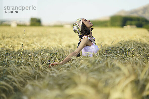 Junge Frau mit Kopftuch steht mit geschlossenen Augen in einem Weizenfeld