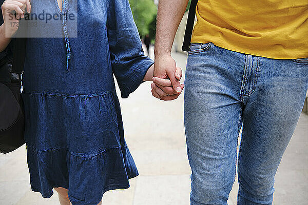 Junges Paar hält sich beim gemeinsamen Spaziergang im Park an den Händen