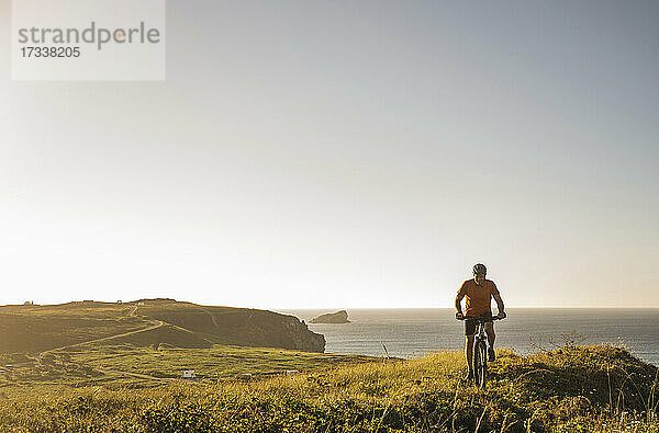 Männlicher Sportler fährt Fahrrad in grüner Landschaft am Meer
