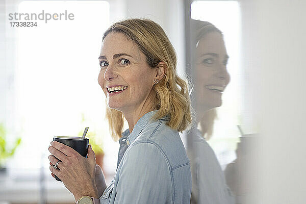 Lächelnde blonde Frau hält Tasse zu Hause