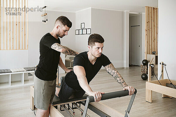 Männlicher Fitnesstrainer bietet Unterstützung  während ein Mann im Studio Pilates praktiziert
