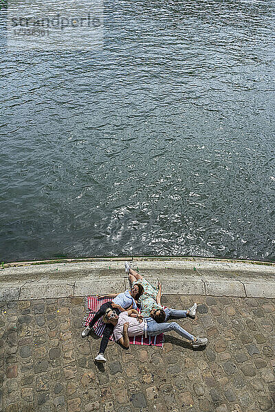 Männliche und weibliche Freunde liegen auf der Promenade am Fluss