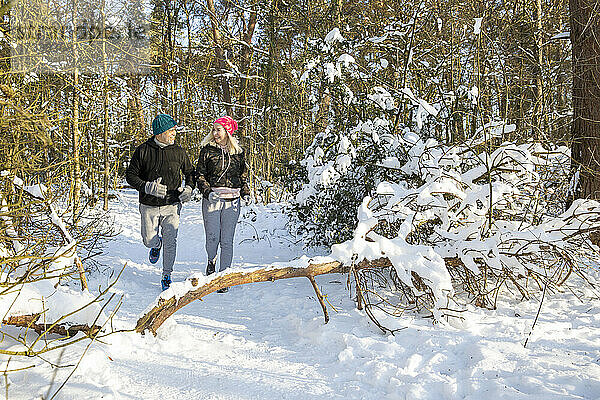 Aktives älteres Paar  das an einem sonnigen Tag im Schnee im Wald läuft
