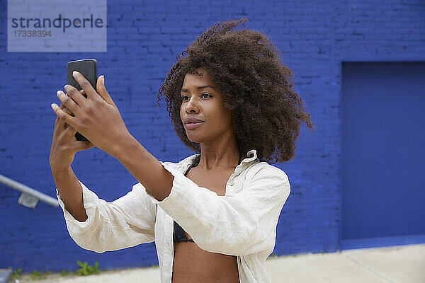 Junge Afro-Frau macht ein Selfie mit ihrem Smartphone vor einer blauen Wand