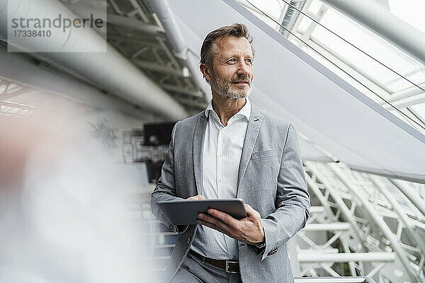 Nachdenklicher männlicher Fachmann  der ein digitales Tablet hält  während er im Büro steht