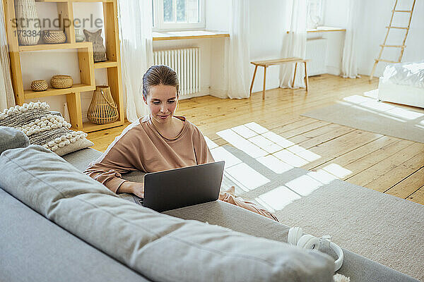 Junge Geschäftsfrau  die einen Laptop benutzt  während sie zu Hause auf dem Boden sitzt
