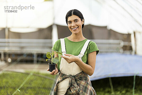 Lächelnde Landarbeiterin stehend mit Topfpflanze