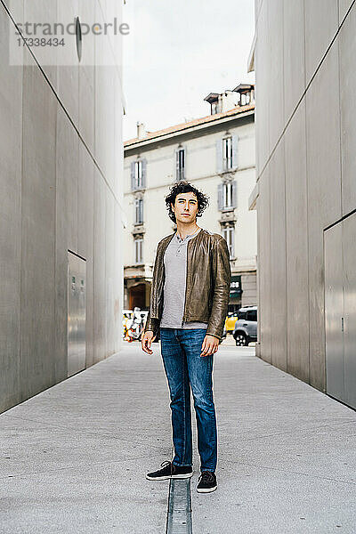 Junger Mann steht auf einem Fußweg inmitten von Gebäuden
