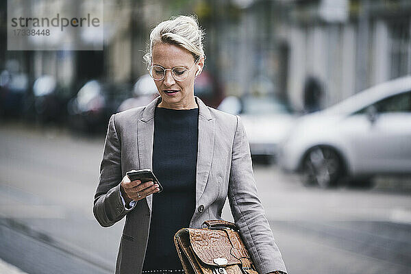 Blonde Pendlerin hält Tasche und benutzt Smartphone