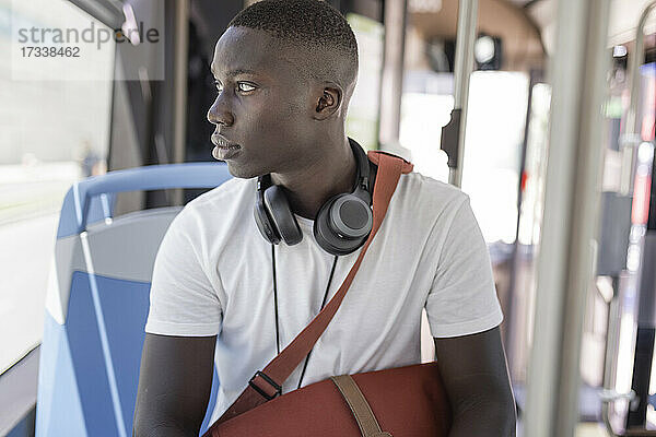 Junger Mann mit Kopfhörern schaut durch ein Fenster im Bus