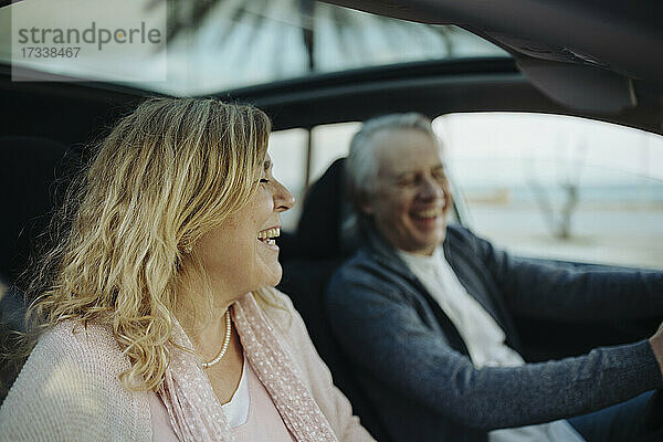 Reife blonde Frau lachend von Mann im Auto sitzend