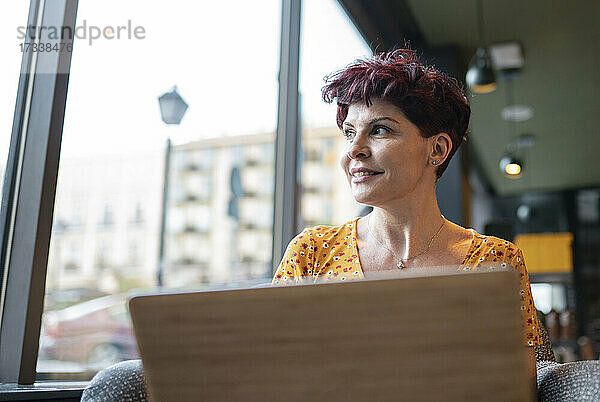 Nachdenkliche Frau  die mit ihrem Laptop in einem Café sitzt und wegschaut